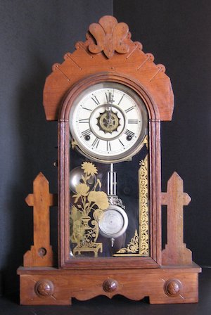 A wooden mantle clock with a white face enclosed in glass with golden design