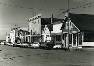 A street lined with buildings, utility poles and parked cars