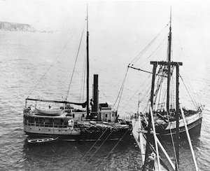 A large steamboat in the water with a chute leading to it from the land for loading cargo