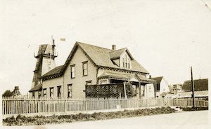 A two-story house with a water tower behind it and a fence in front