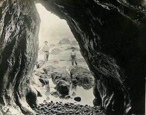 View from inside a cave of a man and child standing in front of the ocean