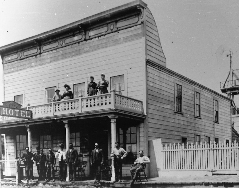 Two-story hotel with balcony. People standing on balcony and sidewalk