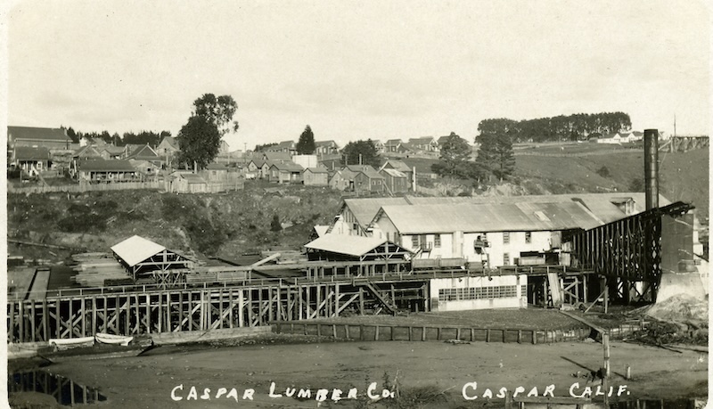 Saw Mill in the foreground. Houses in the background overlook the sawmill.